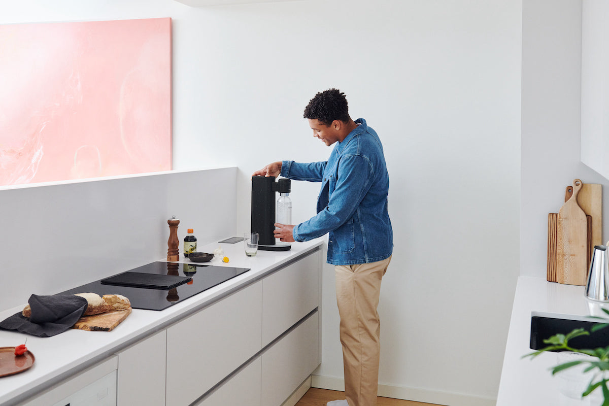 A man making sparkling water with a black Toby soda maker in a white kitchen