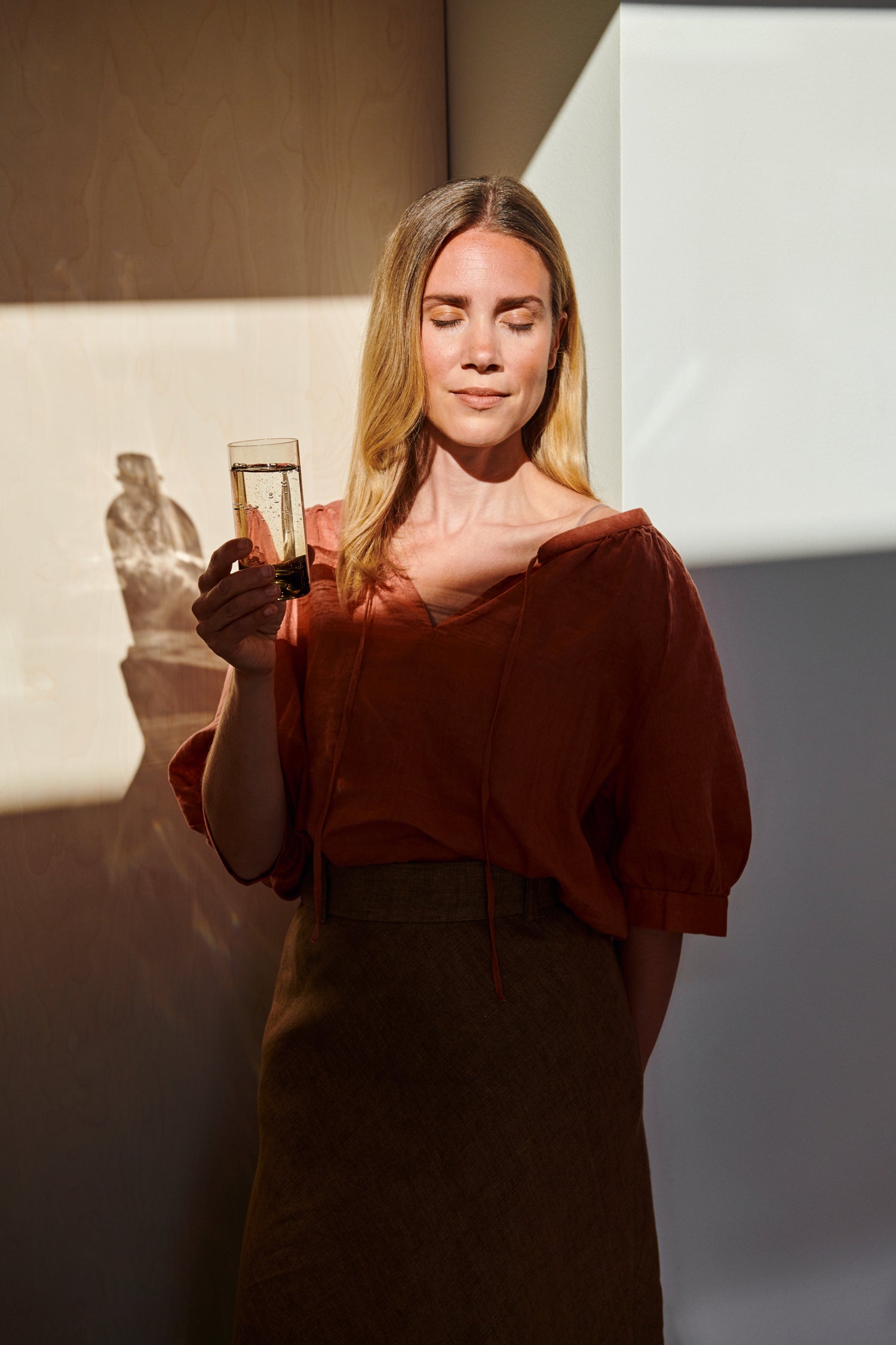 A woman leaning on a wall enjoying sunshine and a glass of sparkling water
