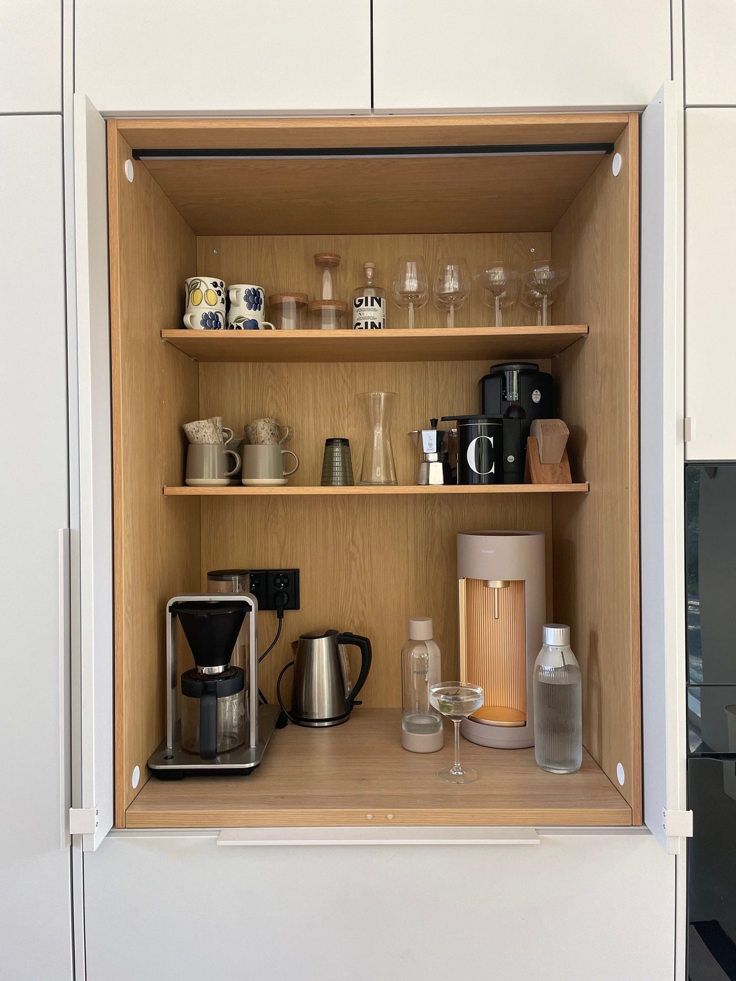 A Glassy sparkling water maker, colour latte in a wood-clad kitchen nook with other drink wear