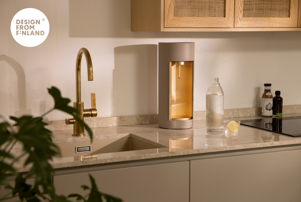 A Glassy soda maker for glass bottles, colour Latte, on the counter in a kitchen light, natural colours. Design from Finland label at the top.