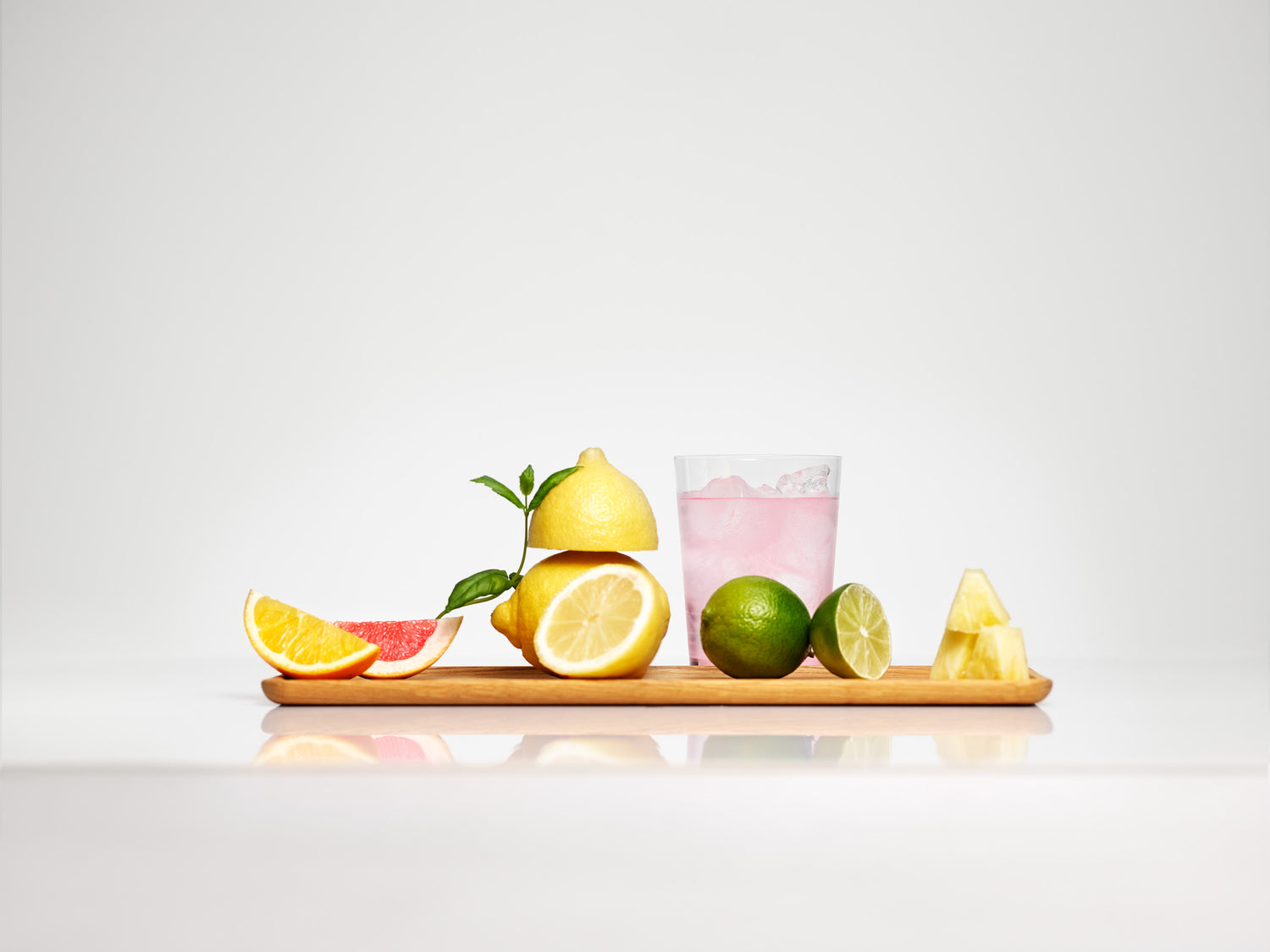 A board with pieces of various citrus fruit and a glass of light pink iced sparkling drink