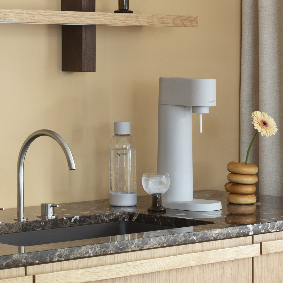 A Woody sparkling water maker in colour Clay and matching water bottle on a dark marble kitchen counter