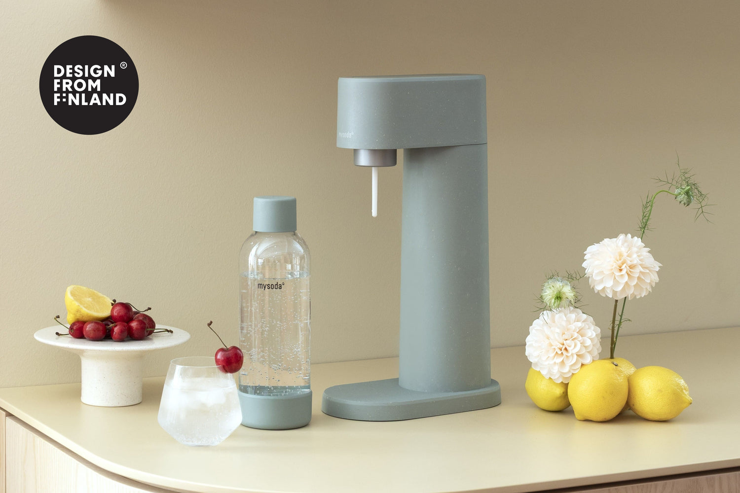 Pigeon Woody soda maker in a summery setting with lemons, cherries and fresh flowers