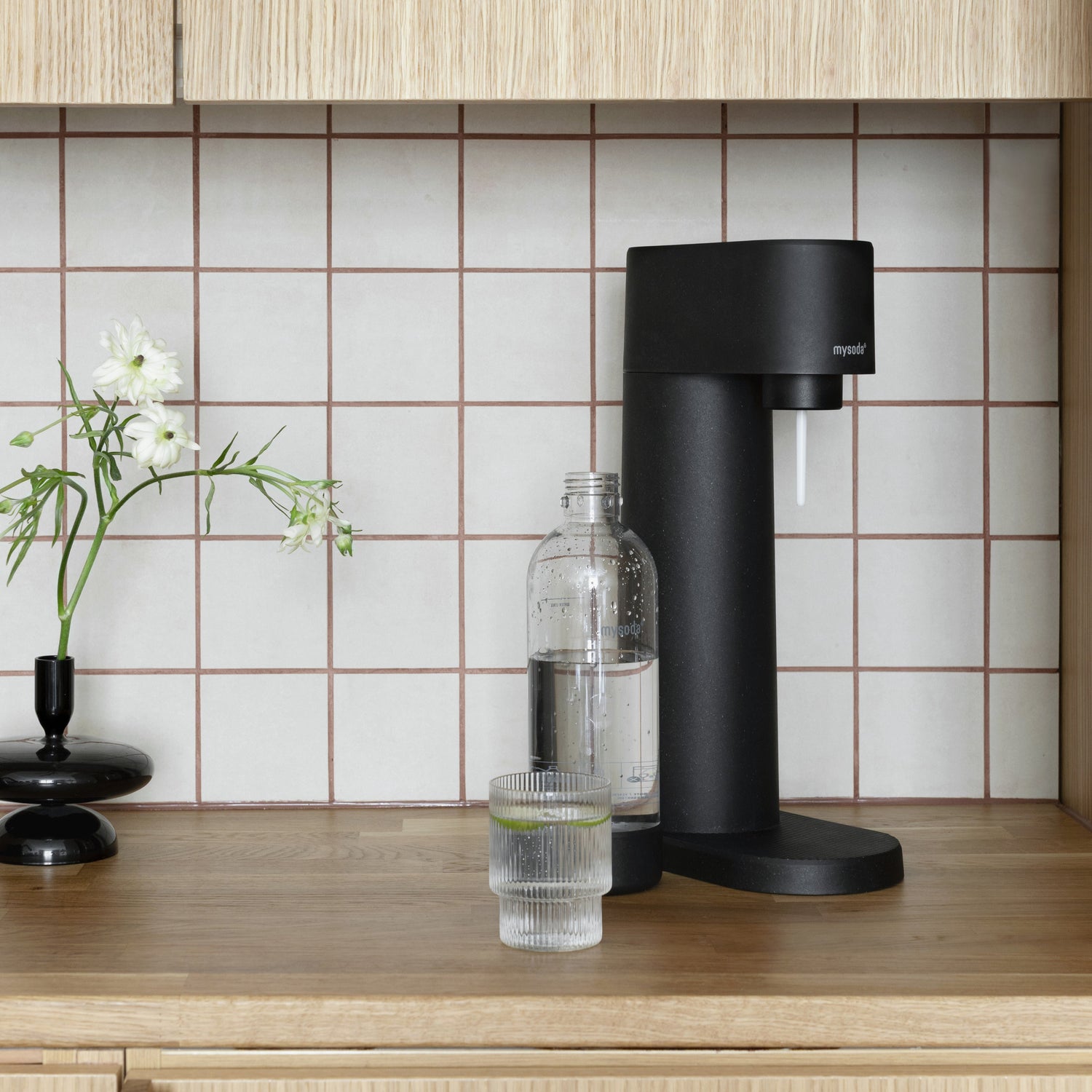 A black Woody sparkling water maker in a kitchen nook clad in timeless white tiles and light wood