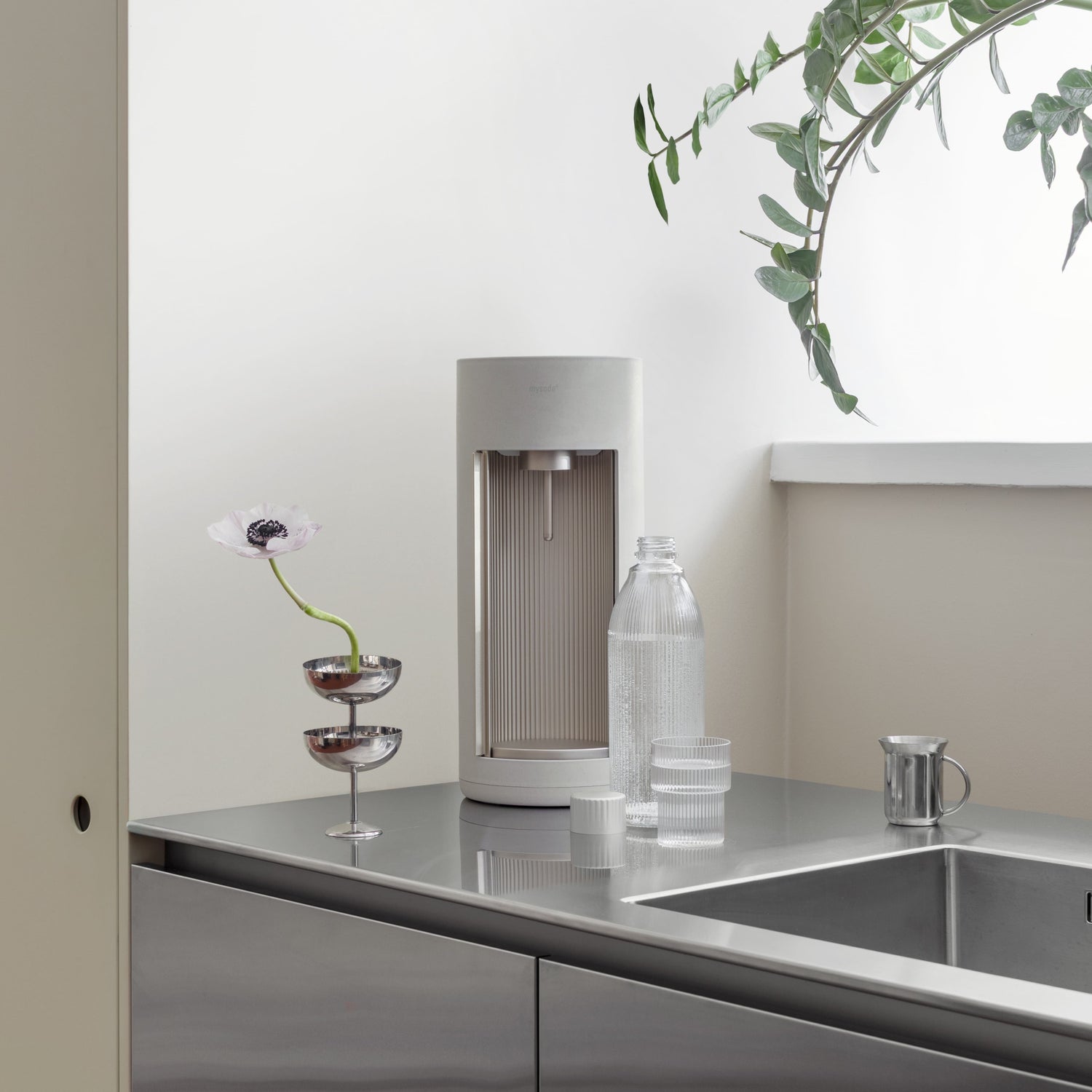 A Glassy sparkling water maker with glass bottle in light clay colour on a stainless steel kitchen counter