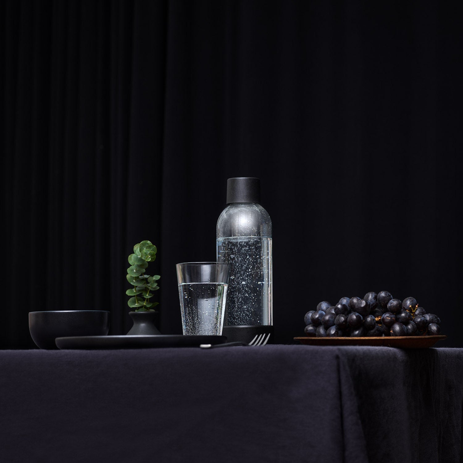A Mysoda water bottle with black cap and bottom in an all-black table setting