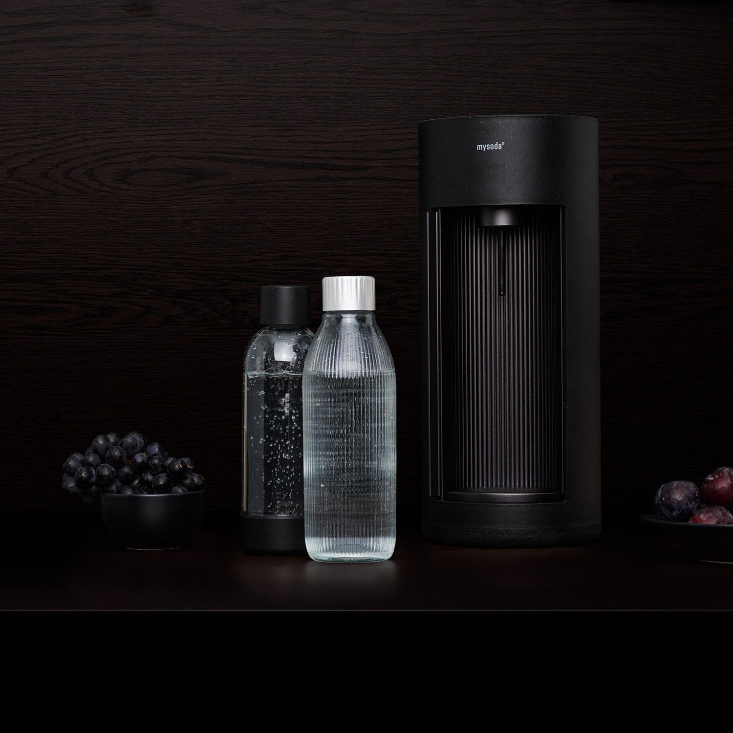 A black Glassy sparkling water maker and glass bottle in front of black background