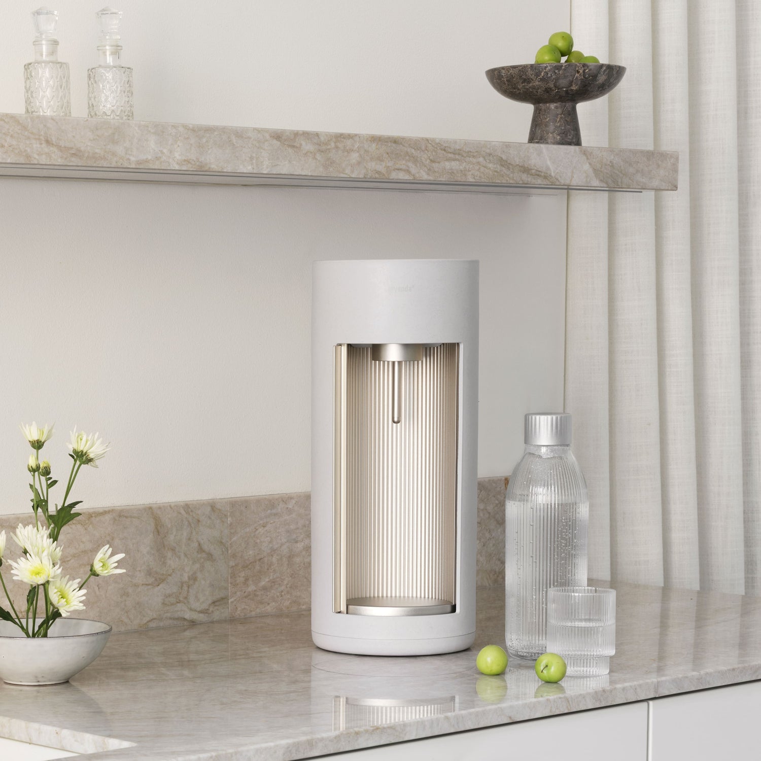 A Glassy soda maker in colour clay with glass bottle and a glass of water in a kitchen held in shades of white and light marble