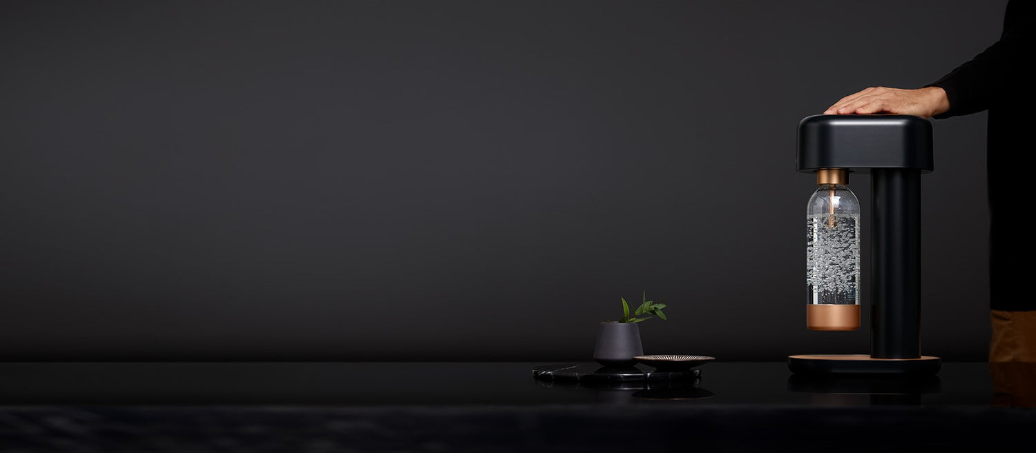 A man resting his hand on a black-copper Ruby 2 soda maker