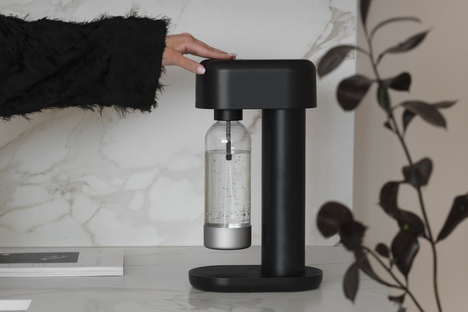 A hand reaching out to carbonate water using Mysoda Ruby soda maker in all black
