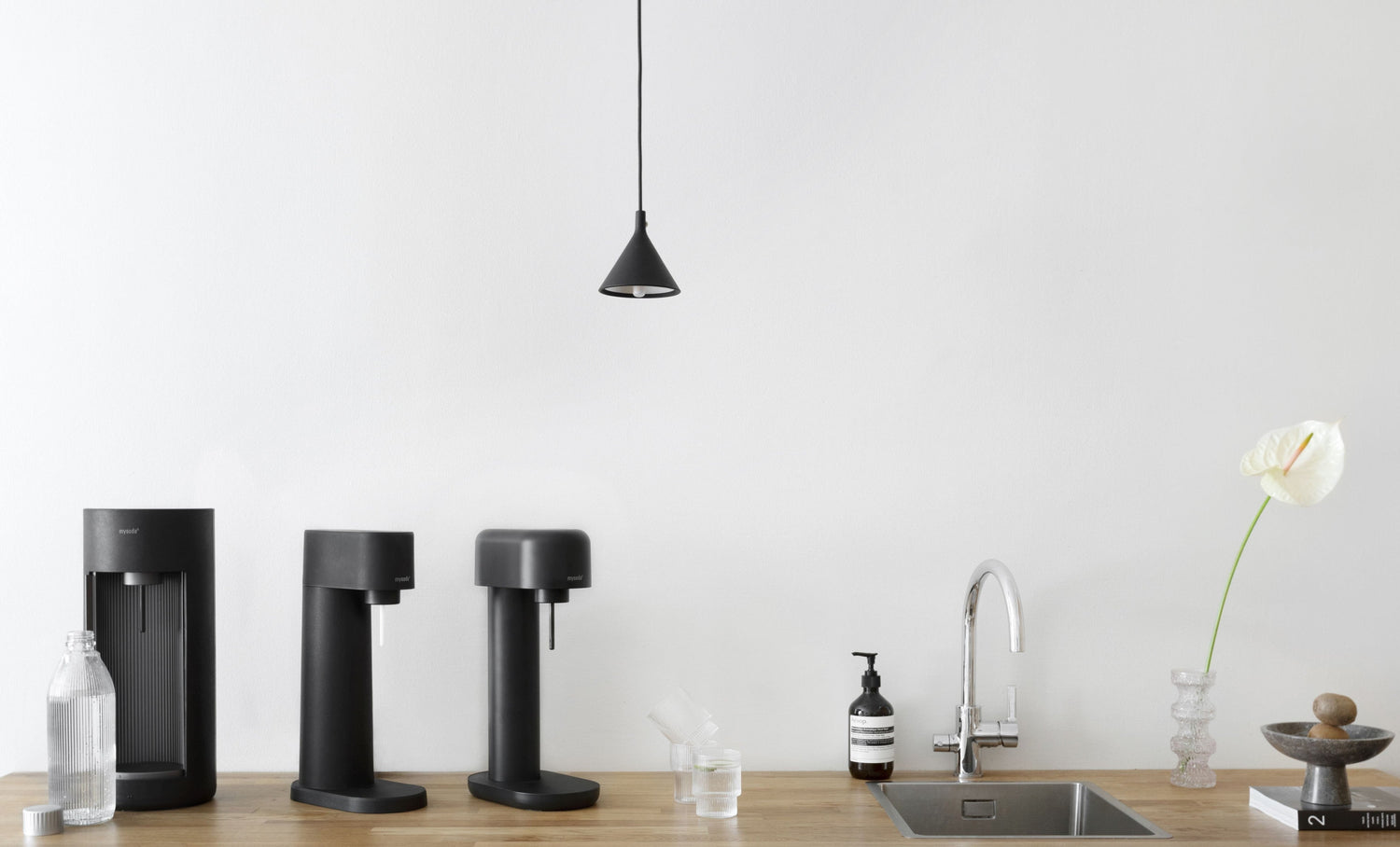Black Glassy, Woody, and Ruby 2 sparkling water makers and matching bottles next to the sink on a wooden kitchen counter