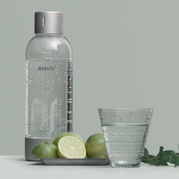 A silver premium bottle, fruit and a glass of water in front of pigeon background#väri_silver