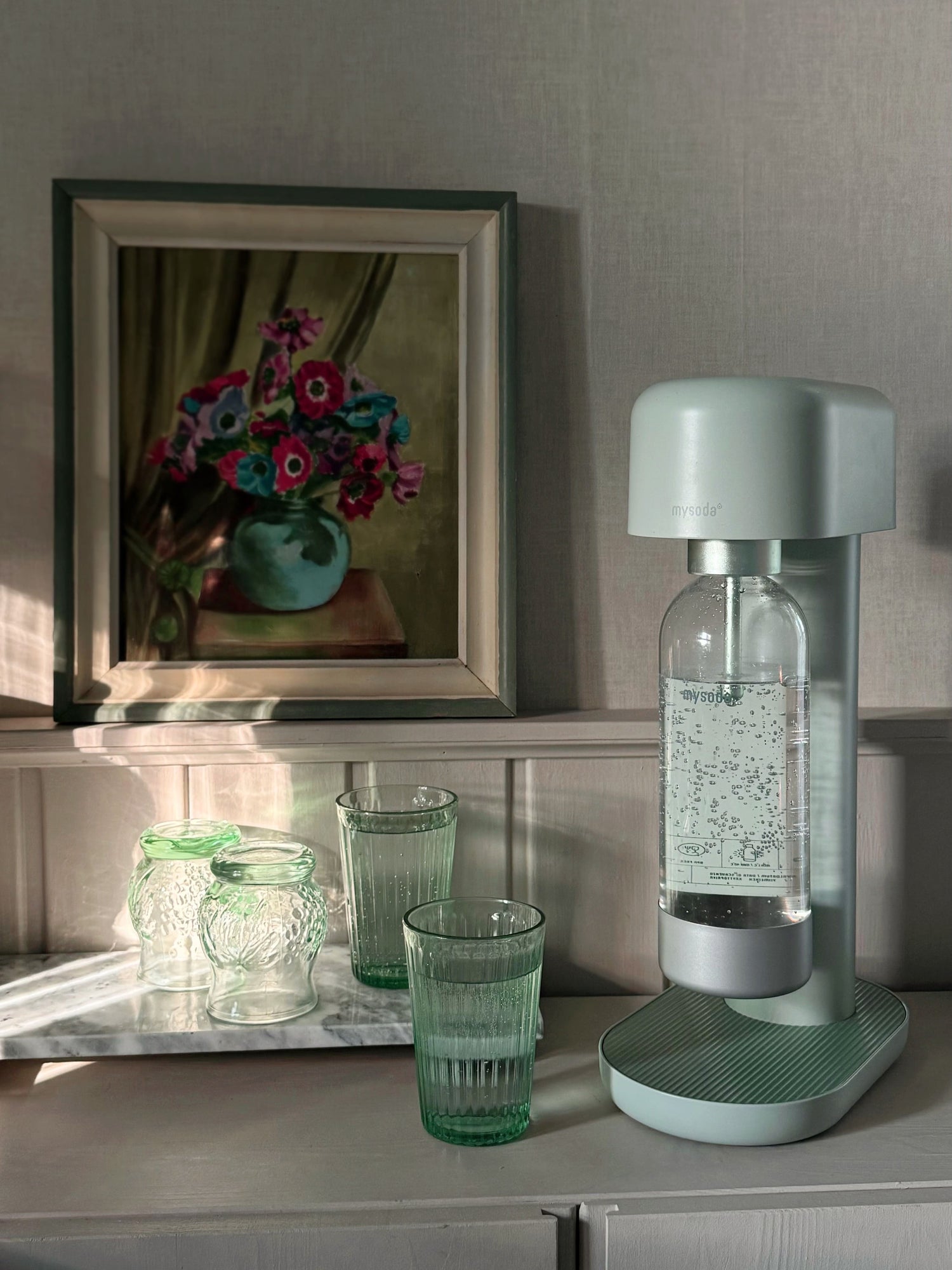 A pigeon/green Ruby 2 sparkling water maker and matching green glasses on a shelf in a traditional cottage