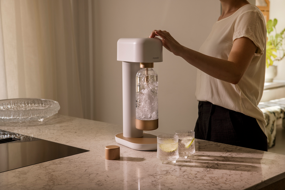 A woman is using a white-copper Ruby 2 soda maker to carbonate water