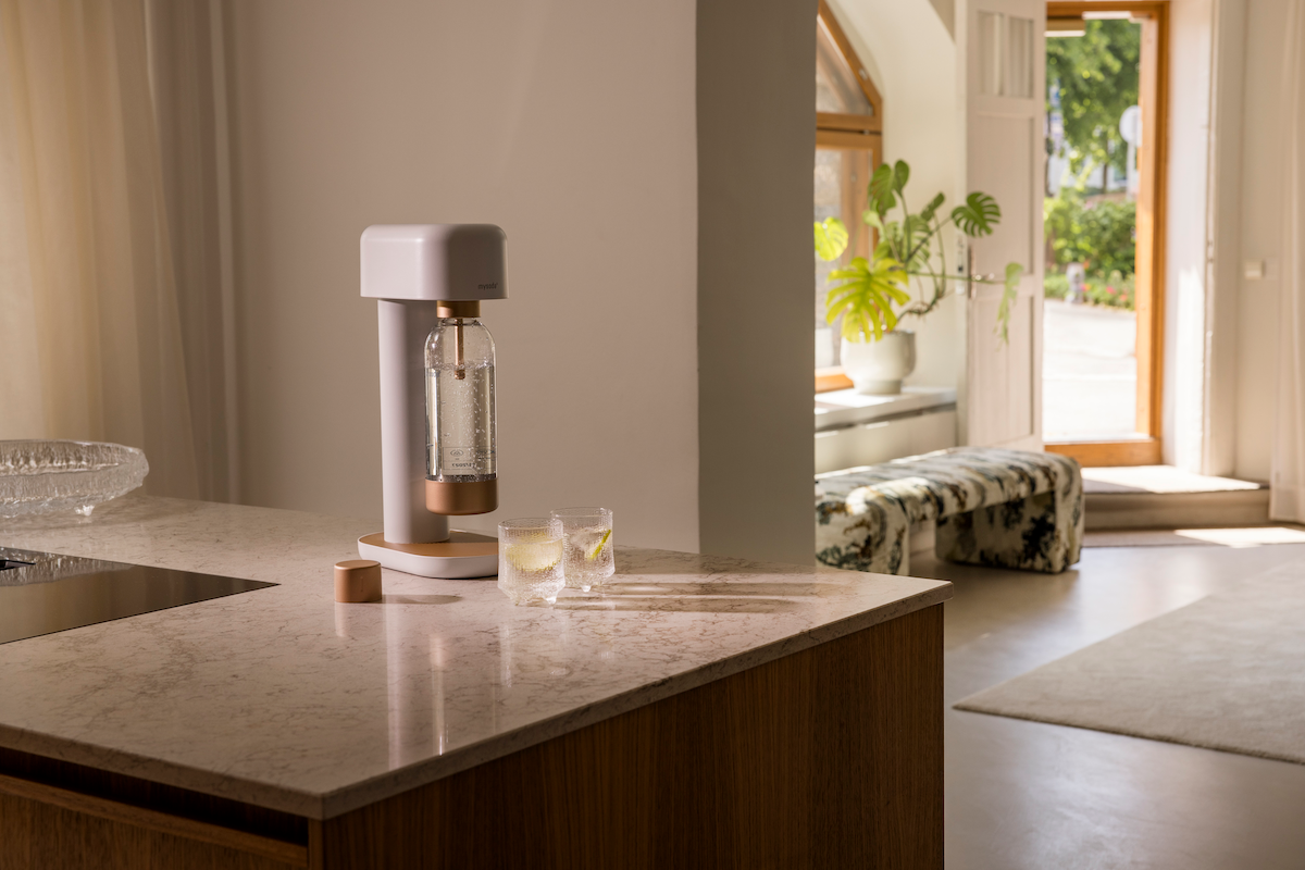 A white-copper Ruby 2 soda maker and two glasses of sparkling water on a marble countertop