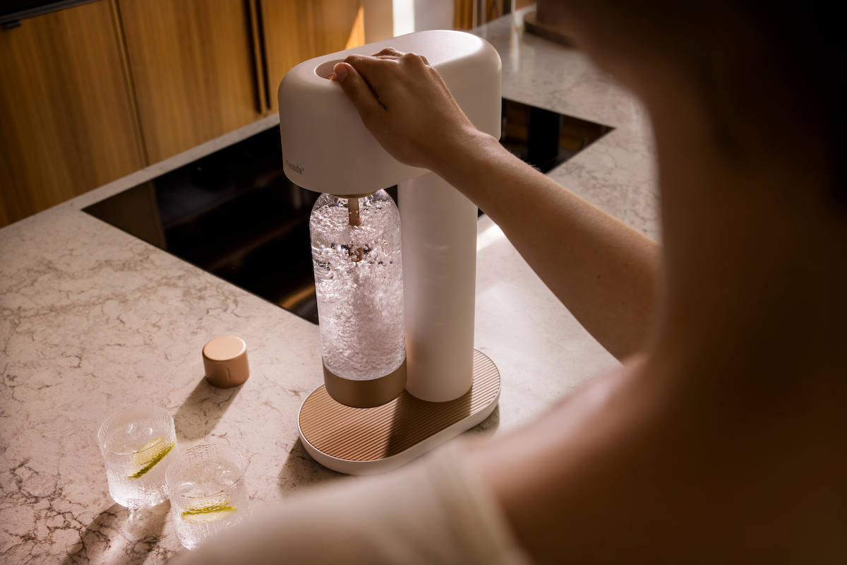 Over-the-sholder view of a woman using a white and copper Ruby 2 sparkling water maker to carbonate fresh water