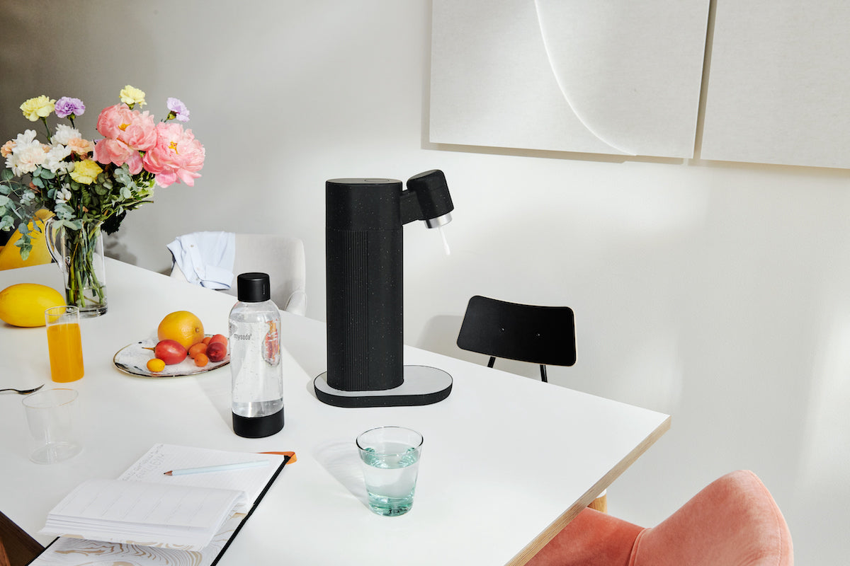 A black Toby soda maker on a white dinner table together with other everyday items