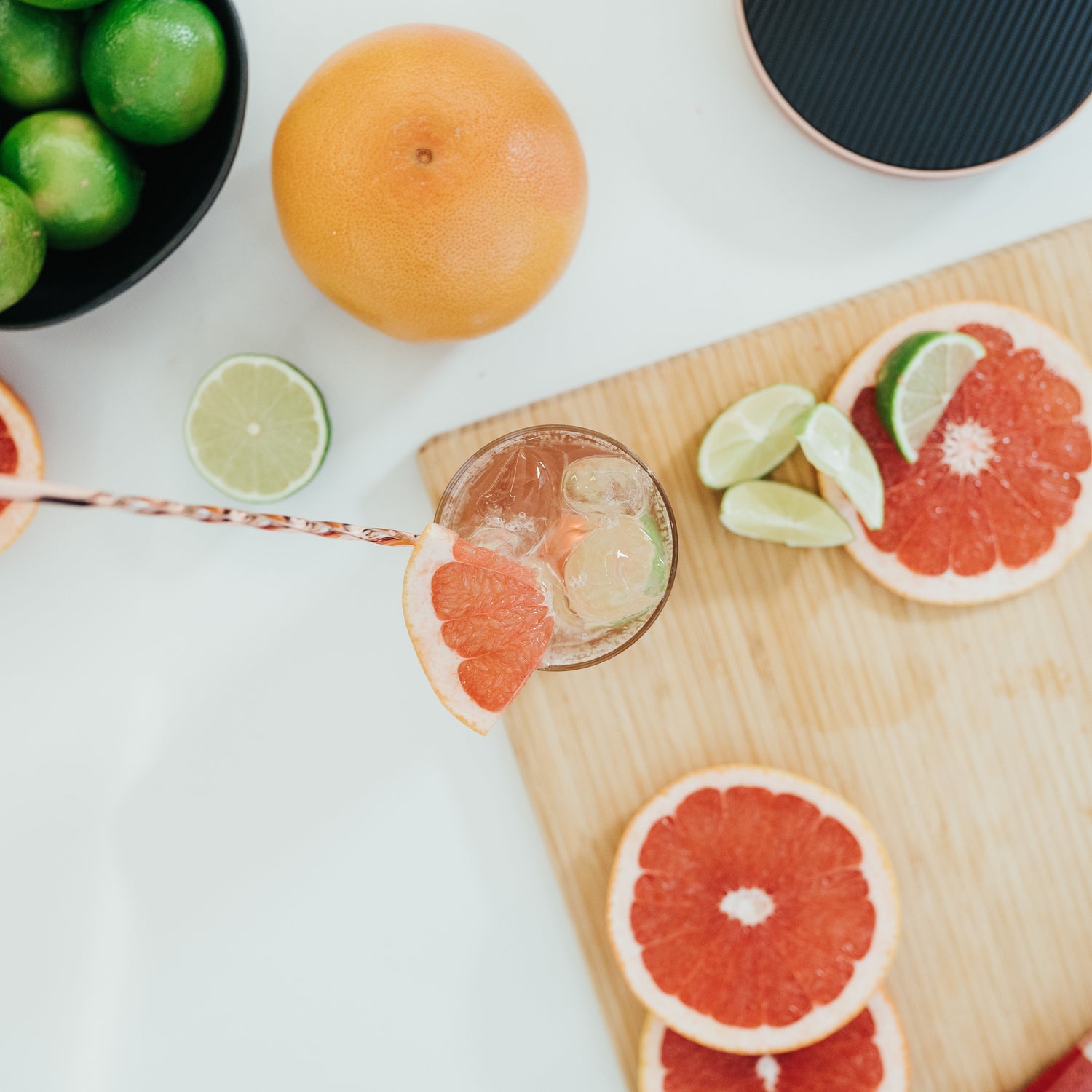 A glass of refrehsing iced grapefruit mocktail on a board with pieces of grapefruit and lime spread around