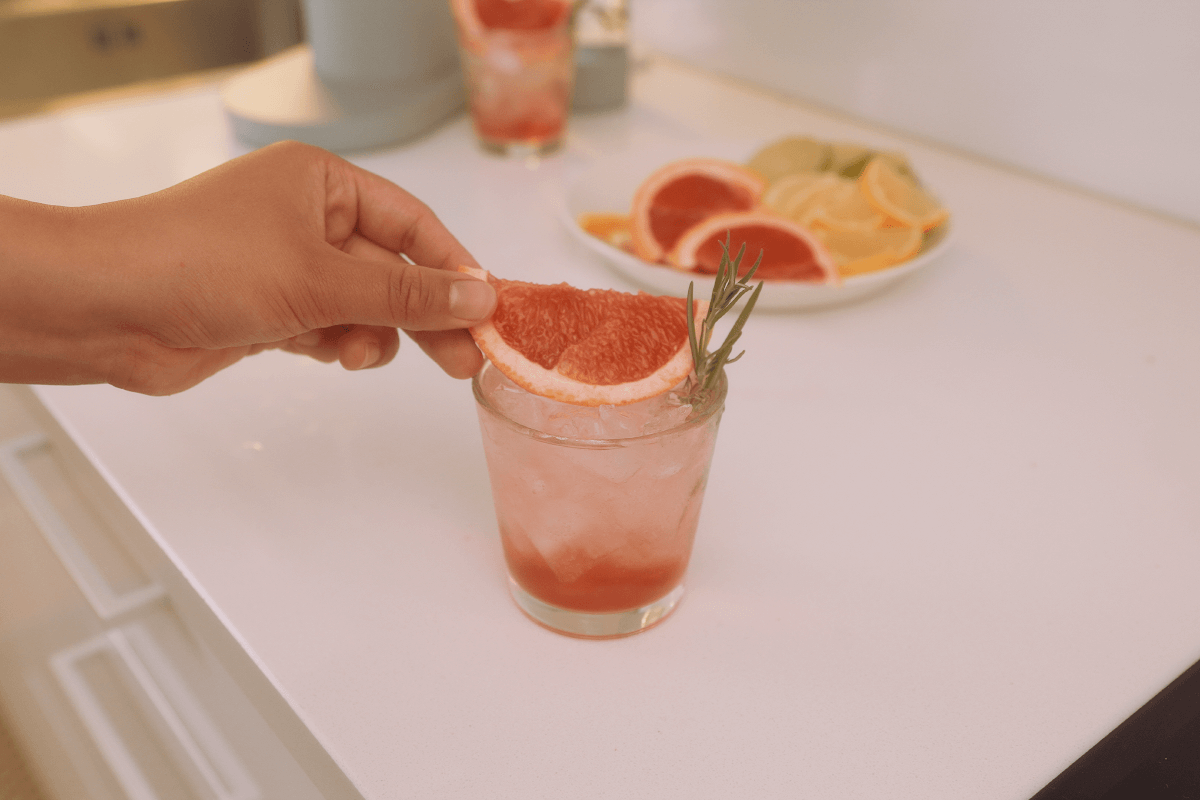 A hand placing a slice of grapefruit on top of a glass of fresh grapefruit drink