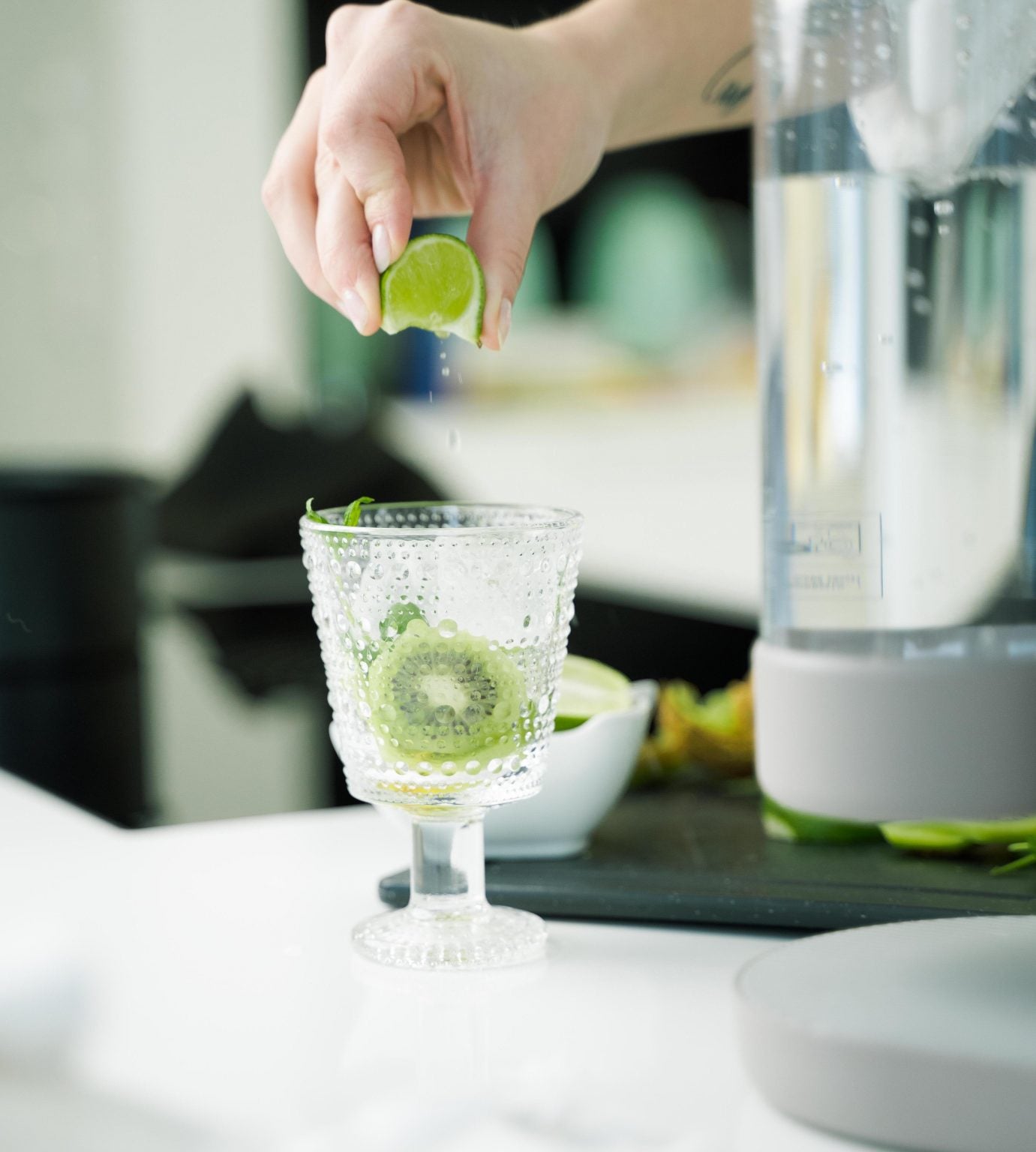 A lime wedge being squeezed out over a glass contianing a kiwi and some herbs