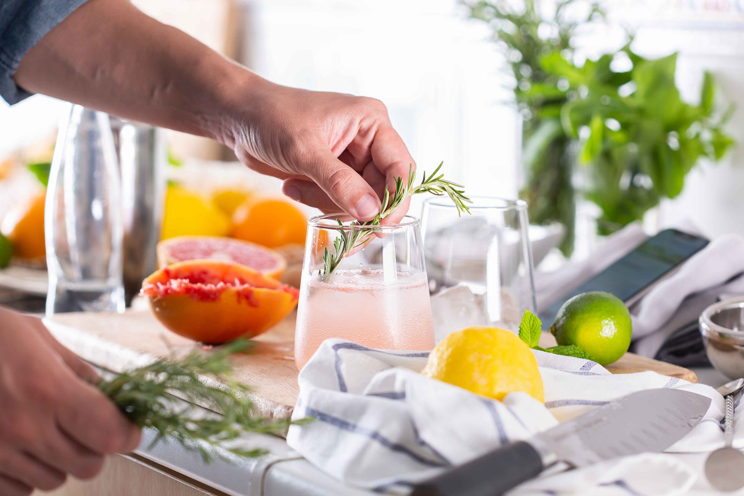 Someone decorating a glass of bubbly citrus drink with a twig of rosemary