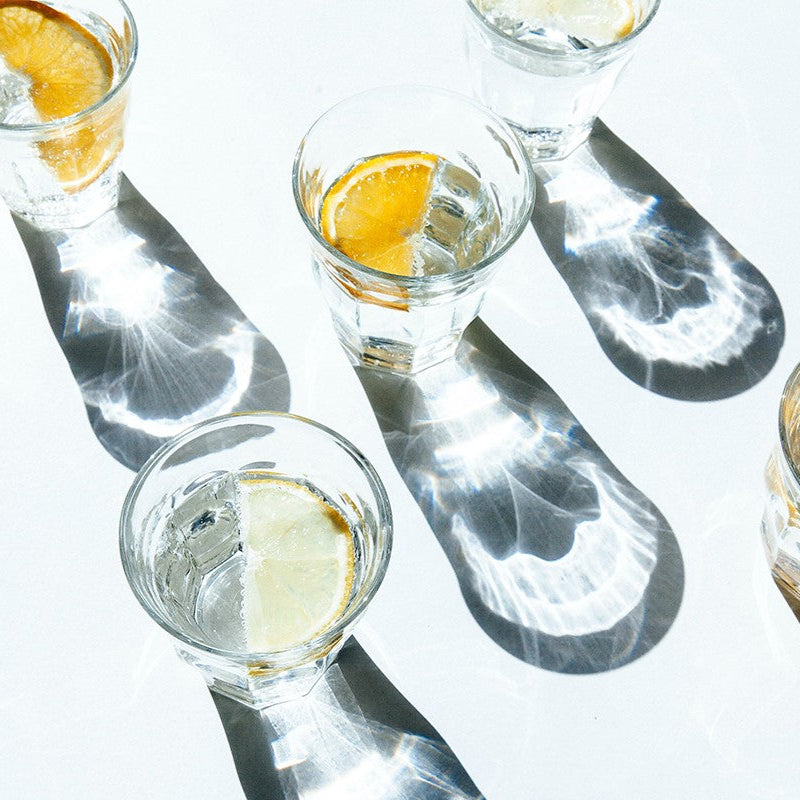 Glasses of sparkling water decorated with slices of orange and lime. The glasses break the bright sunlight