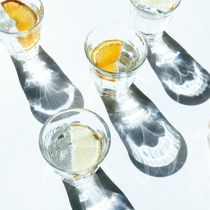 Glasses of sparkling water decorated with slices of orange and lime. The glasses break the bright sunlight