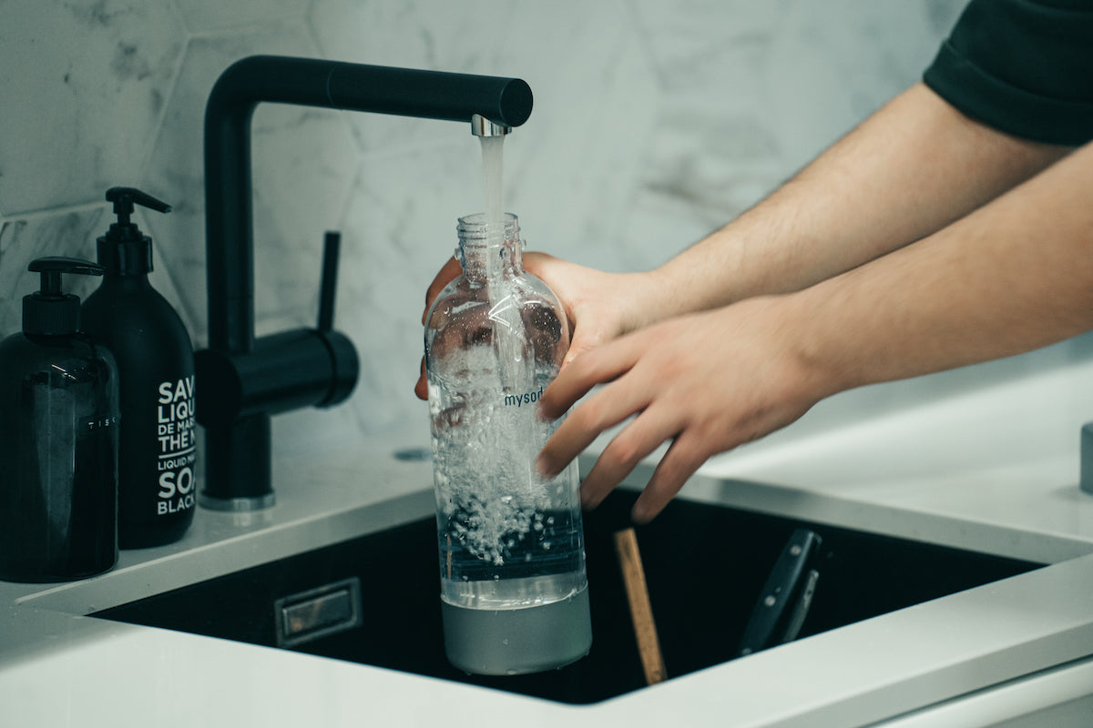 Male arms filling a mysoda PET water bottle at a kitchen sink