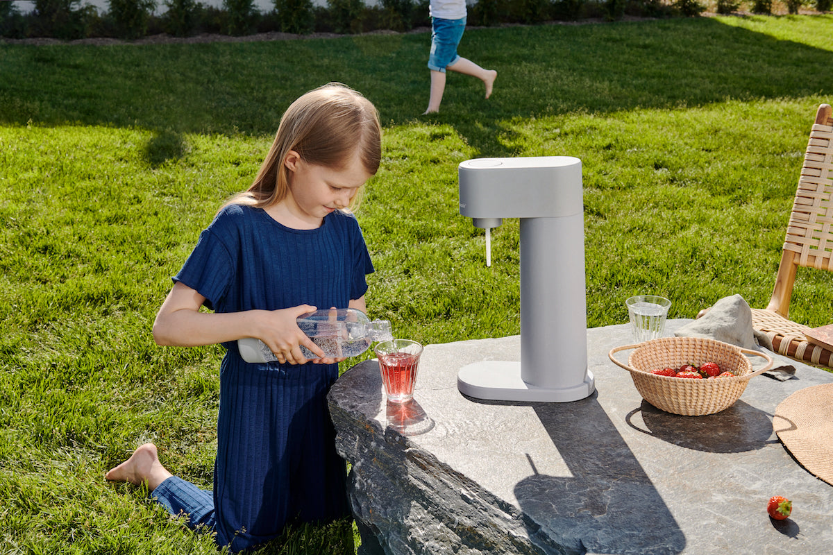 A girl in a garden mixing her drink with Mysoda drink mix and fresh sparkling water maker from the Woody sparkling water maker in front of her
