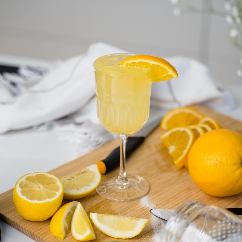 A glass of orange-lemon-mocktail on a board with slices of orange and lemon spread around it