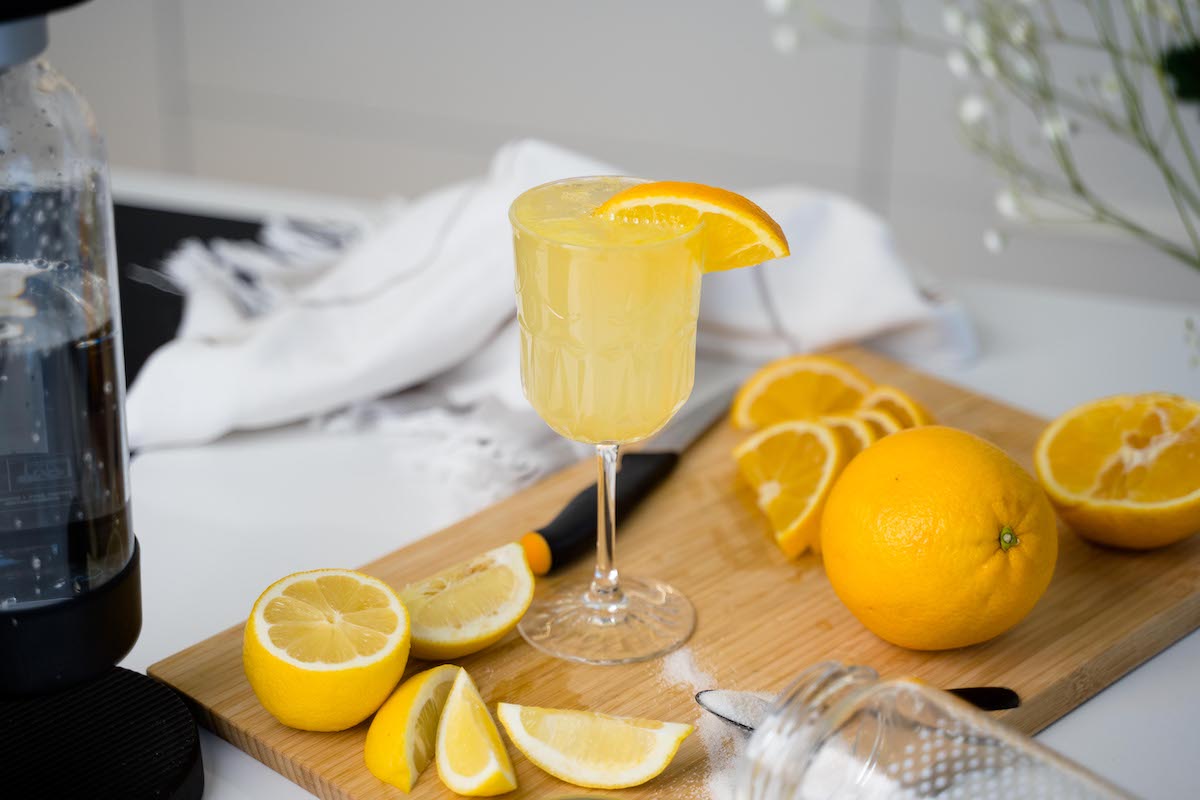 A glass of orange lemon bubbly drink on a wooden board surrounded by pieces of fresh lemon and orange