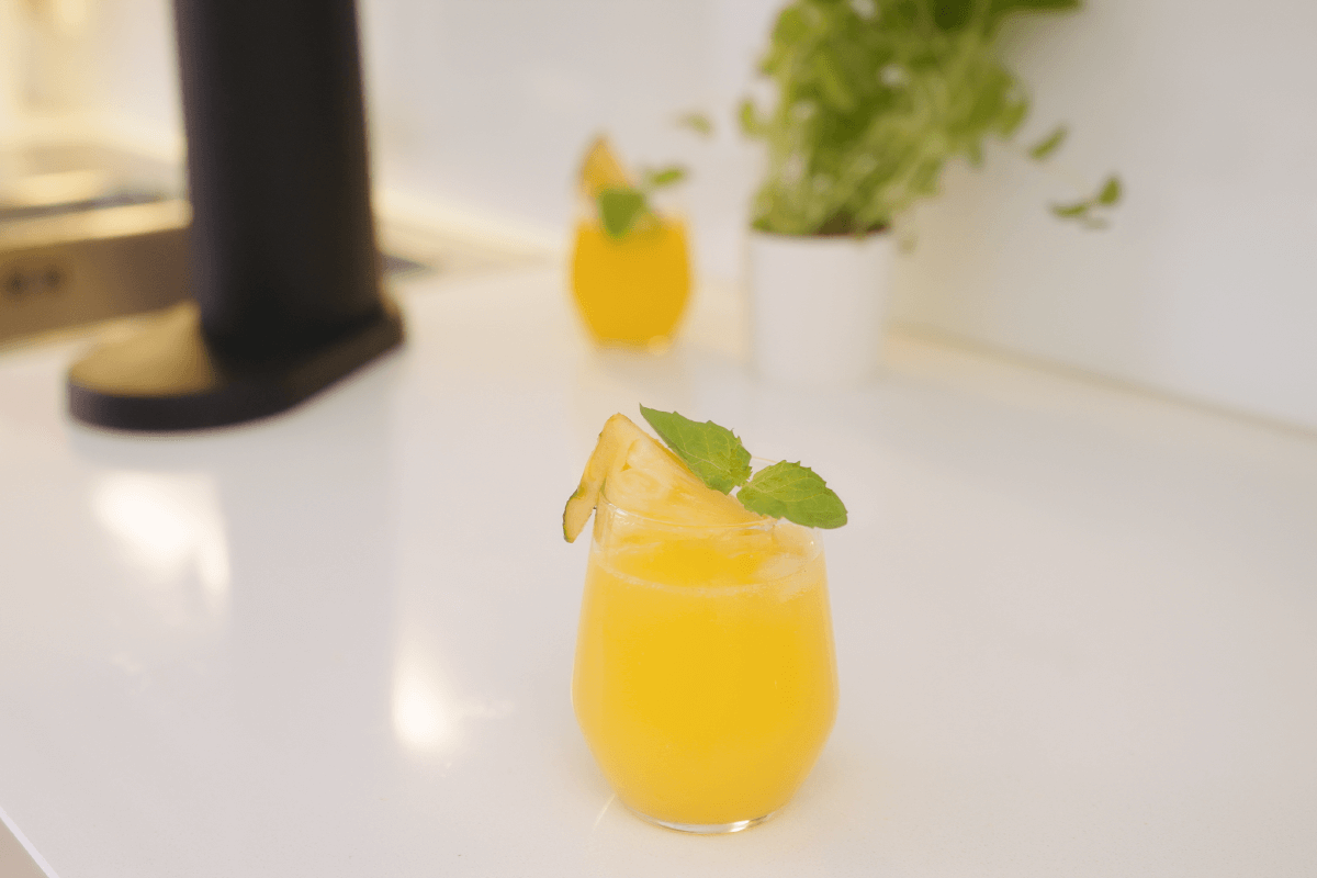A glass of bright yellow pineapple mocktail on a white surface