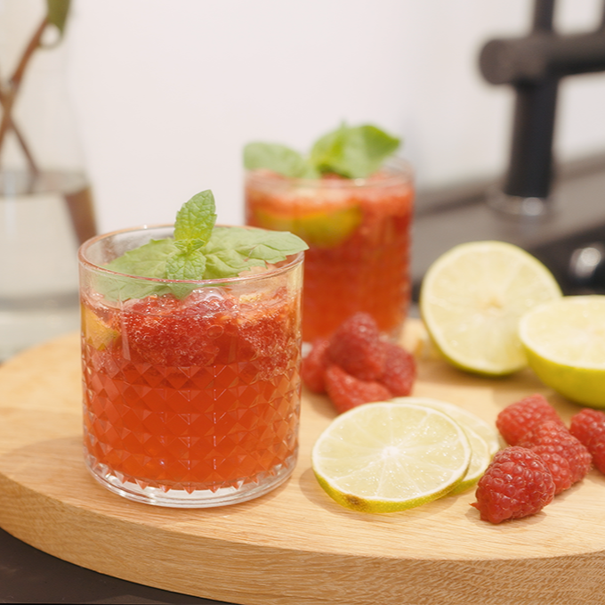 Two glasses of alcohol-free raspberry-lime-cocktail with raspberries and slices of lime on a board