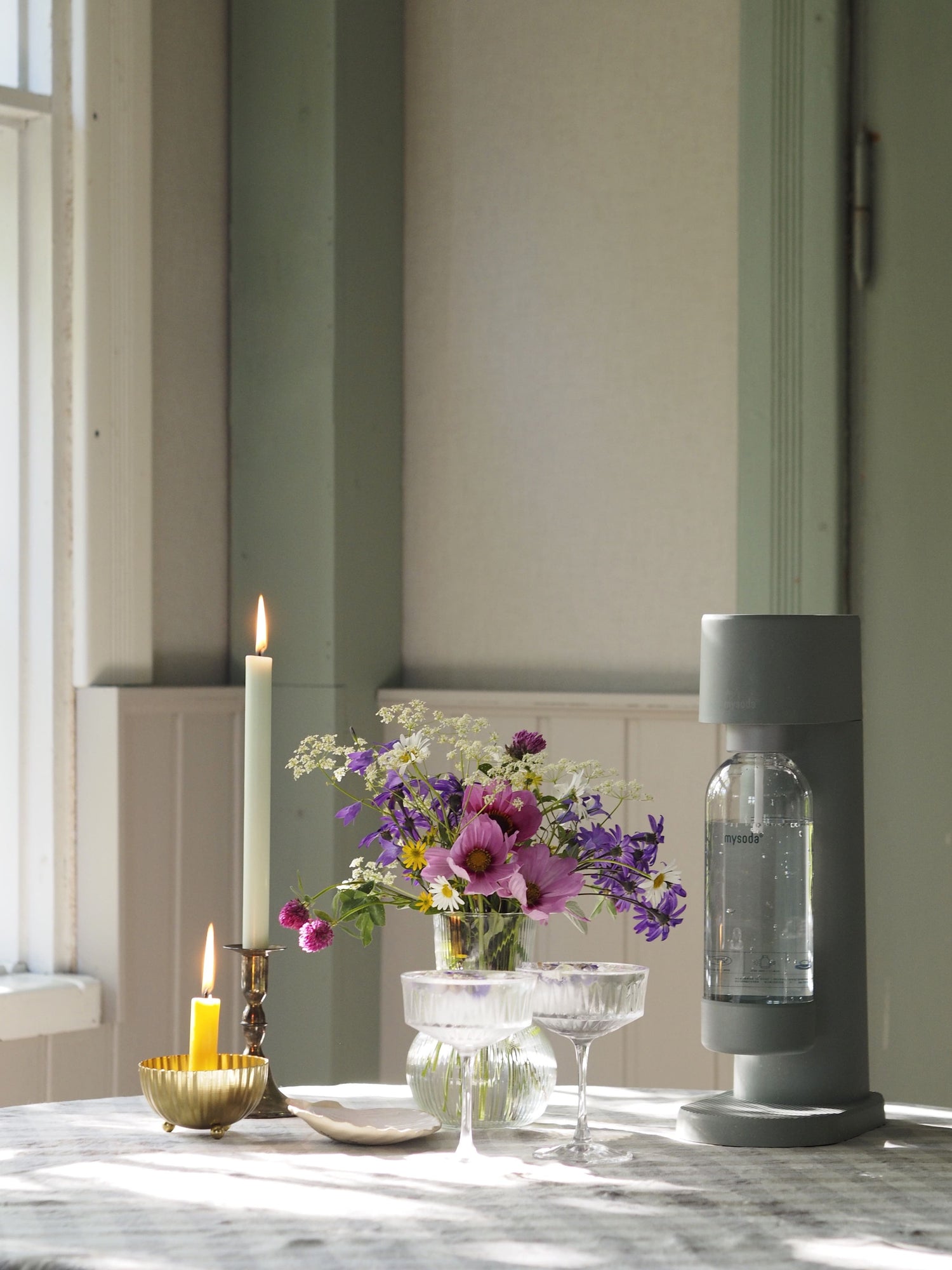 A pigeon Woody soda maker with colourful wildflowers, candles and drinking glasses on a table in a country house
