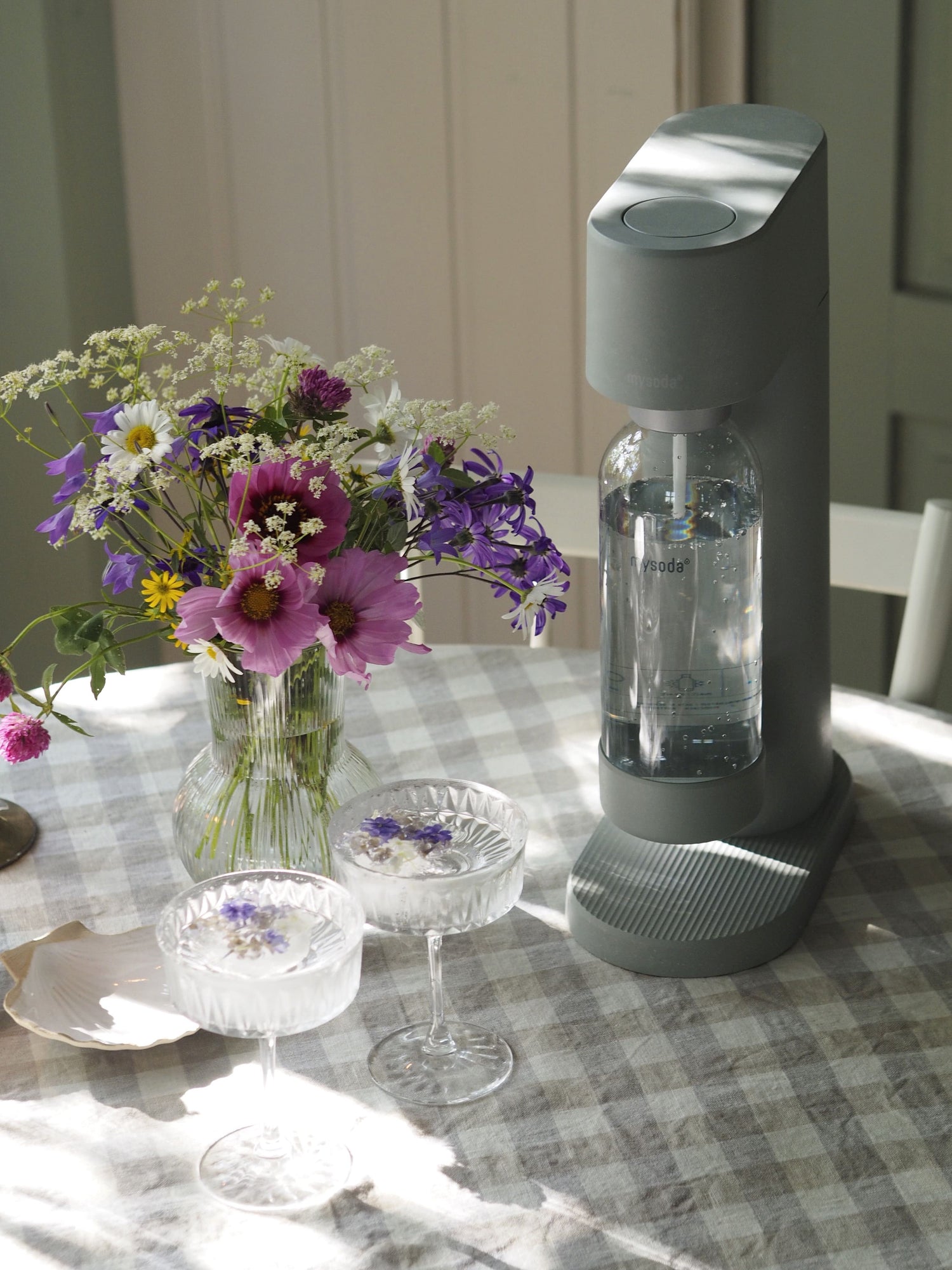 A pigeon Woody soda maker with colourful wildflowers, and drinking glasses on a table in a country house