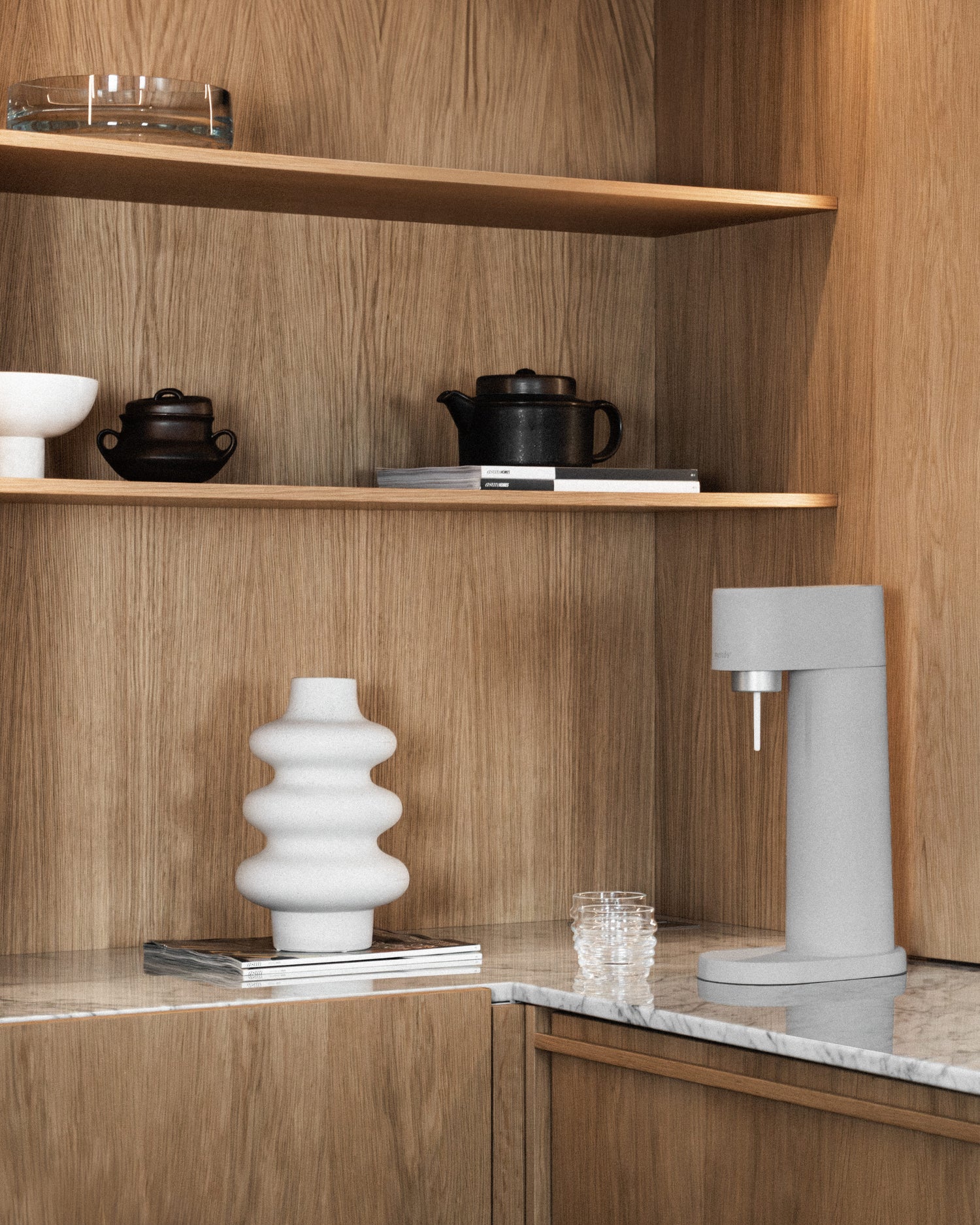 A gray Woody sparkling water maker on white marble counter in a wood-clad corner shelf