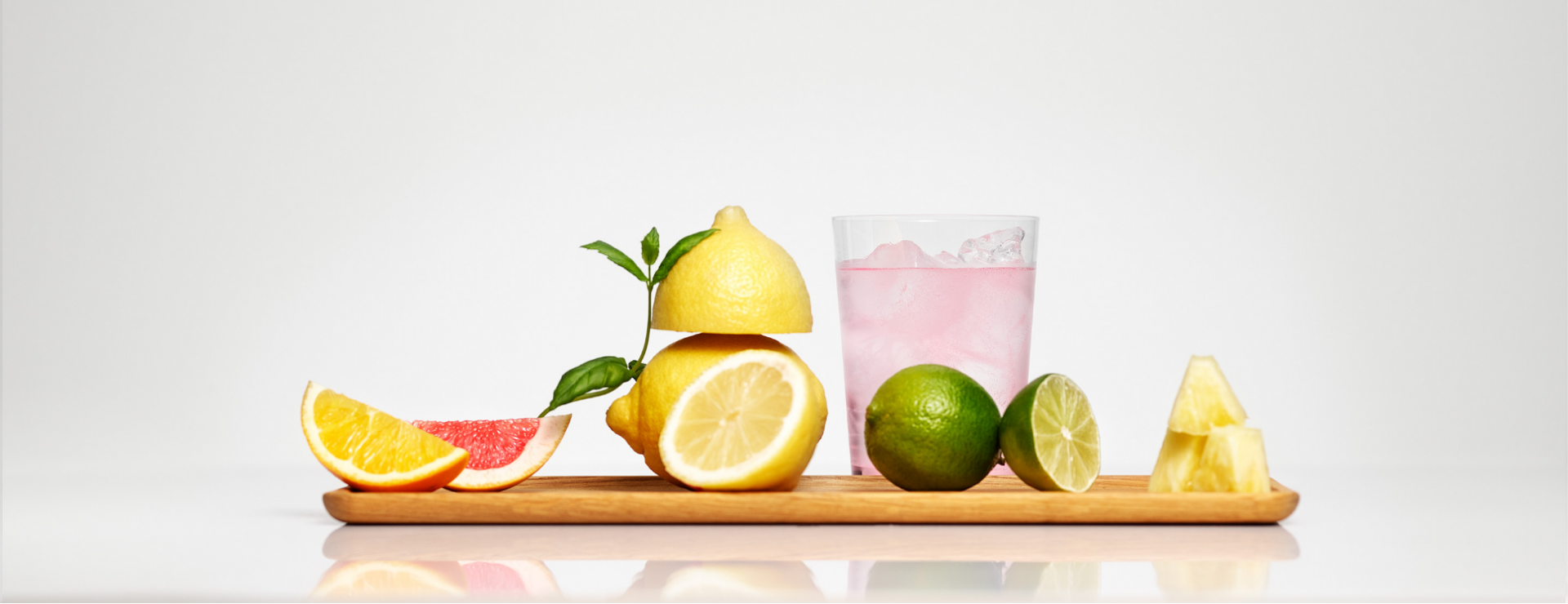 A glass of Mysoda sparkling drink on a board full of citrus fruit and pineapple pieces in a minimalistic setting in front of a white background