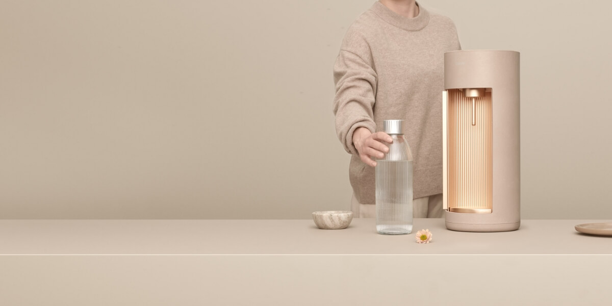 Une machine à eau pétillante latte Mysoda Glassy et une bouteille en verre devant un fond latte.