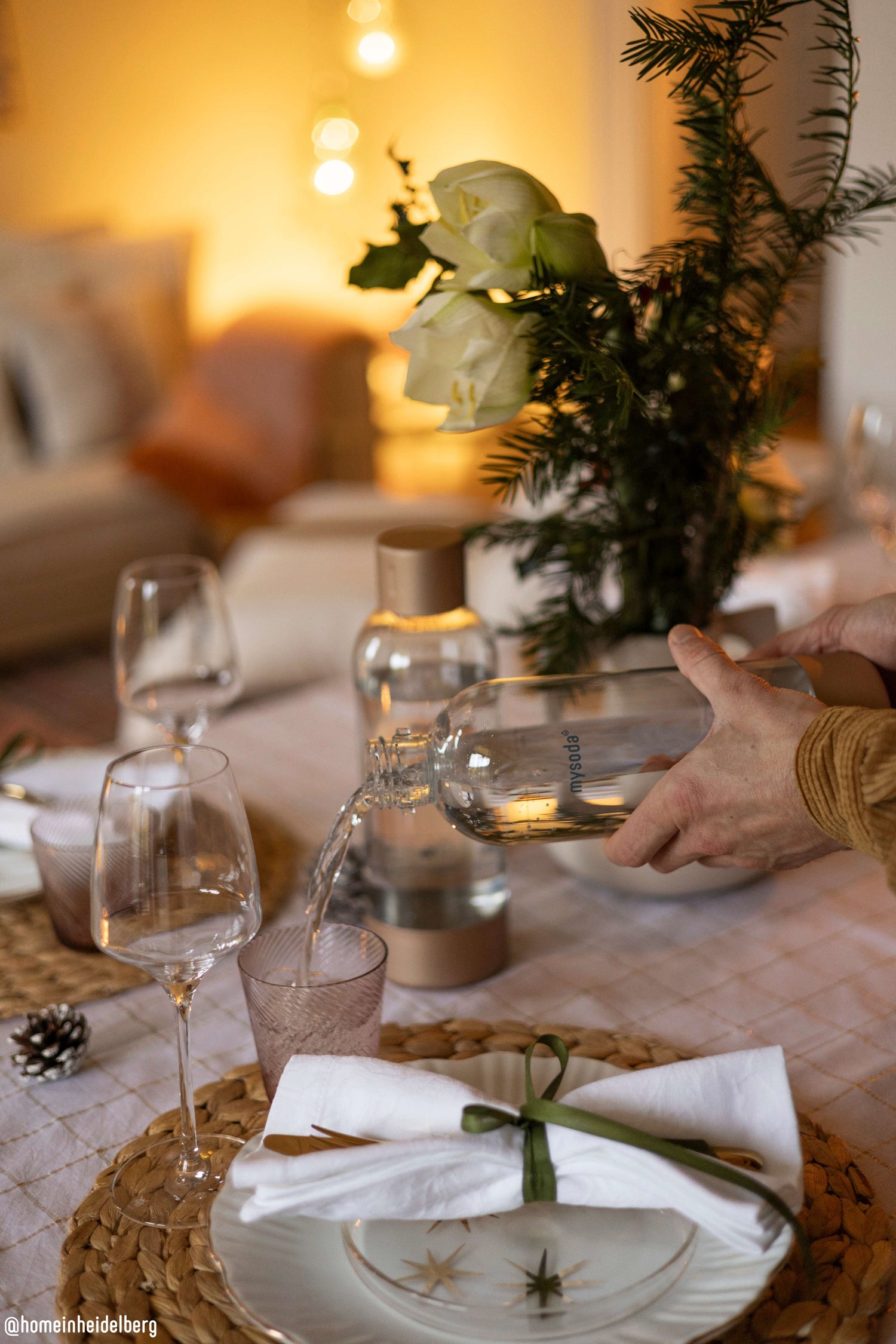 A festive Christmas dinner table in warm colours with a man pouring water from a water bottle