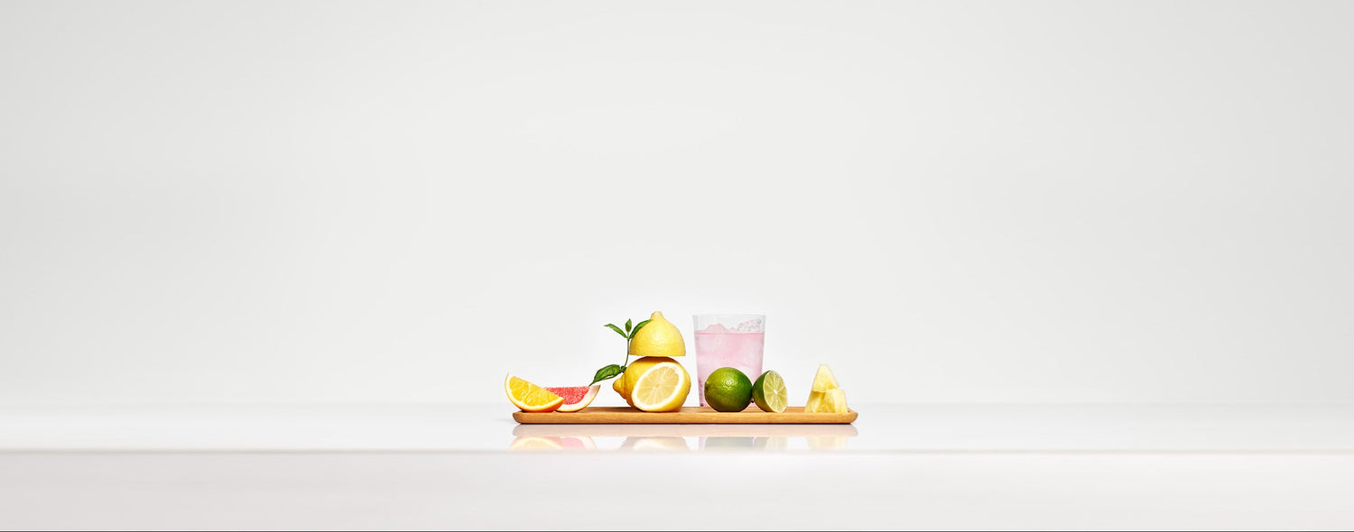 A board with pieces of various citrus fruit and a glass of light pink iced sparkling drink