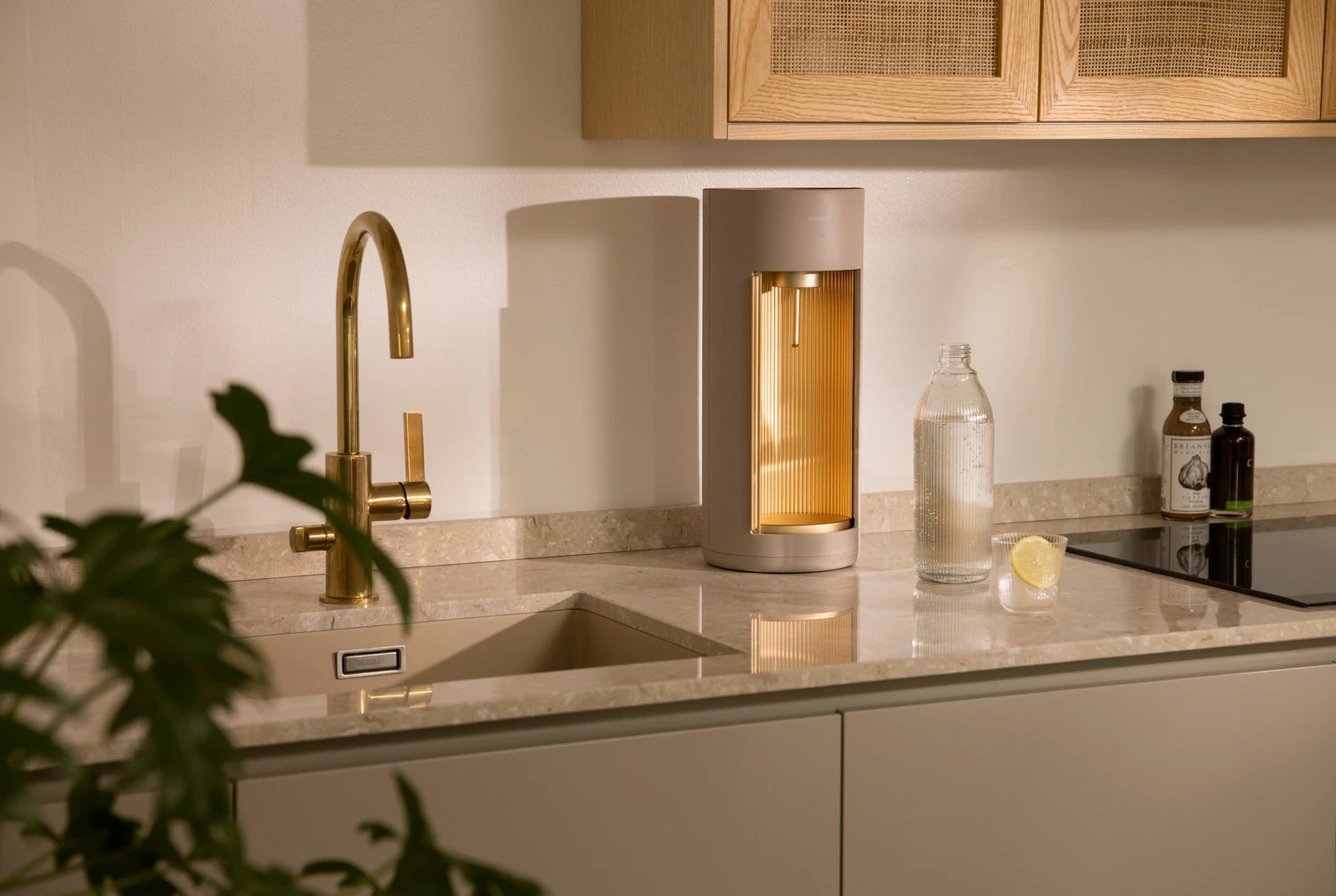 A Glassy sparkling water maker - colour option latte -, a glass bottle, and a glass of sparkling water on a kitchen counter