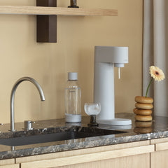 A Woody sparkling water maker in colour Clay and matching water bottle on a dark marble kitchen counter