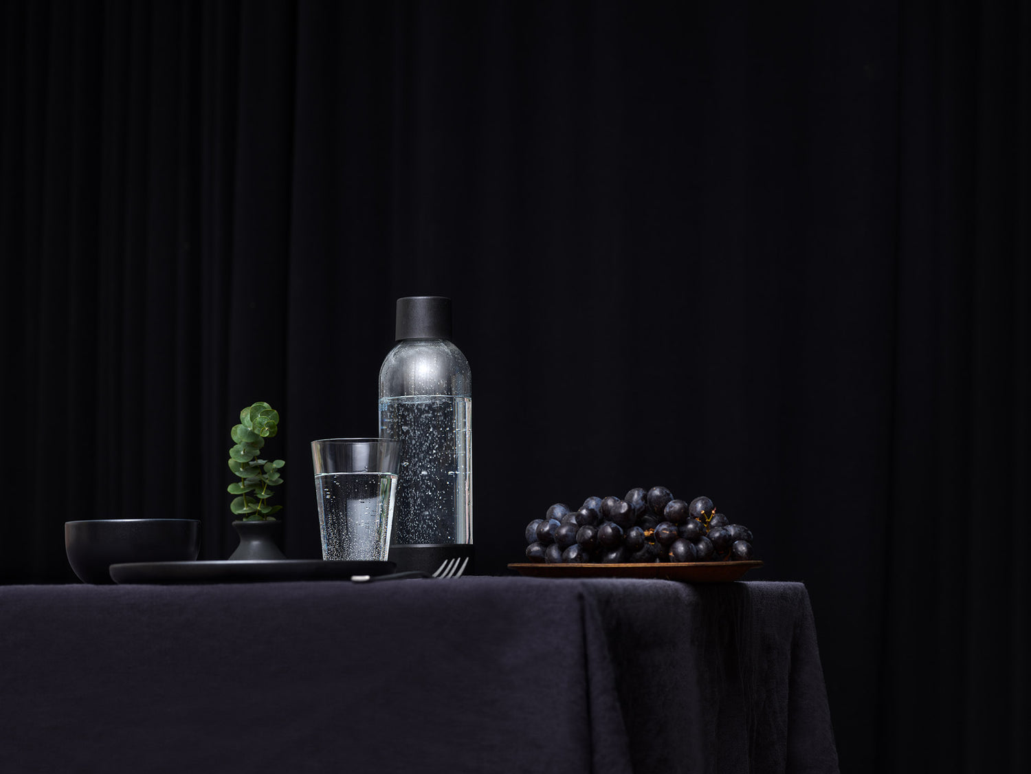 A Mysoda water bottle with black cap and bottom in an all-black table setting