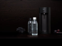 A black Glassy sparkling water maker and glass bottle in front of black background