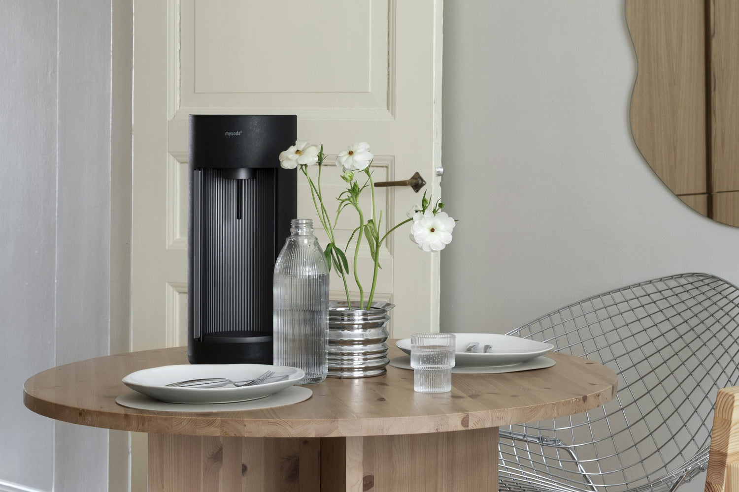 A black Glassy sparkling water maker in a table setting with glass bottle, minimalist Scandinavian decor and white flowers