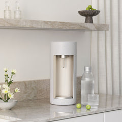 A Glassy soda maker in colour clay with glass bottle and a glass of water in a kitchen held in shades of white and light marble