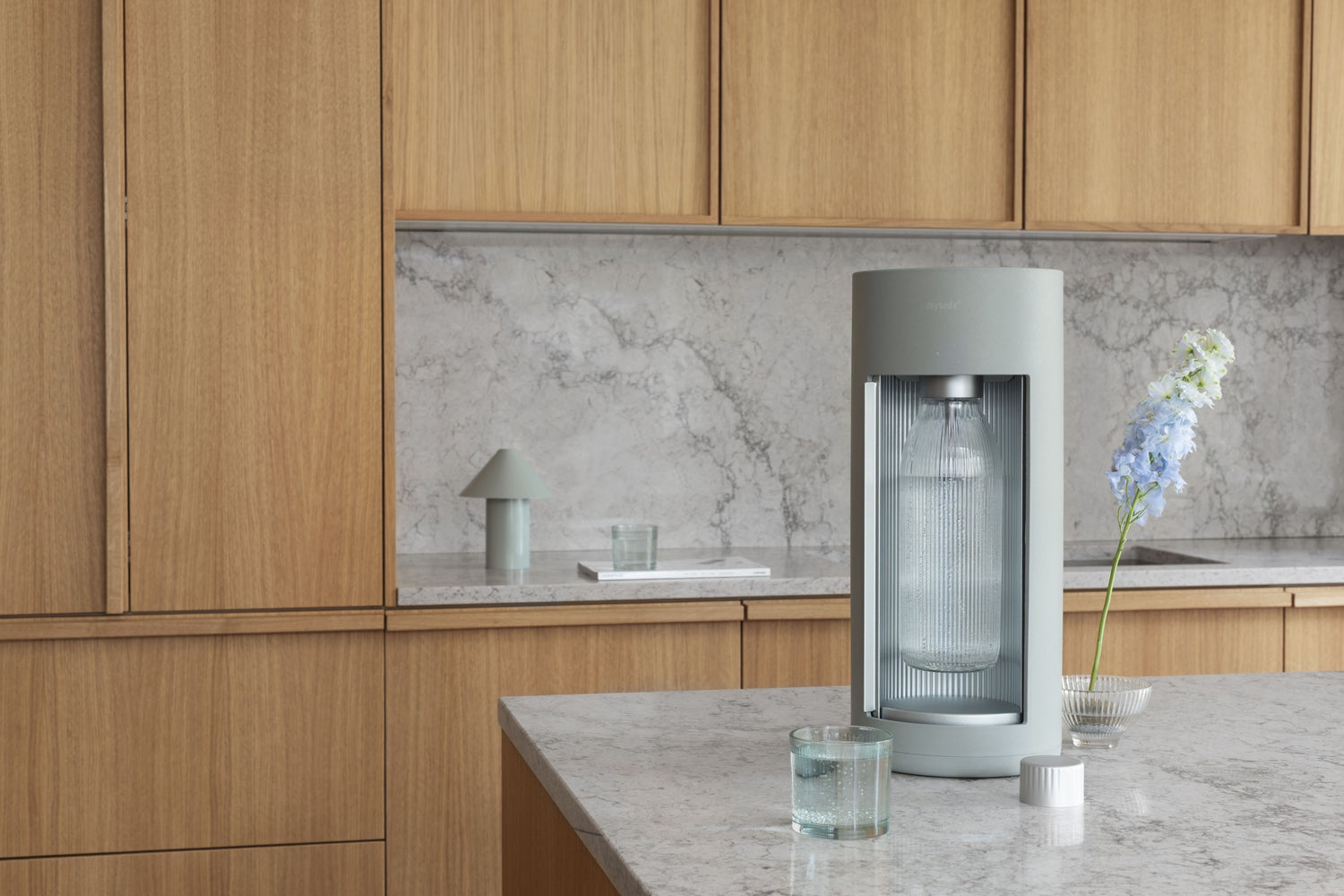 A pigeon coloured Mysoda Glassy carbonator in an elegant, minimalistic kitchen with gry marble counters and wooden closets in light colour