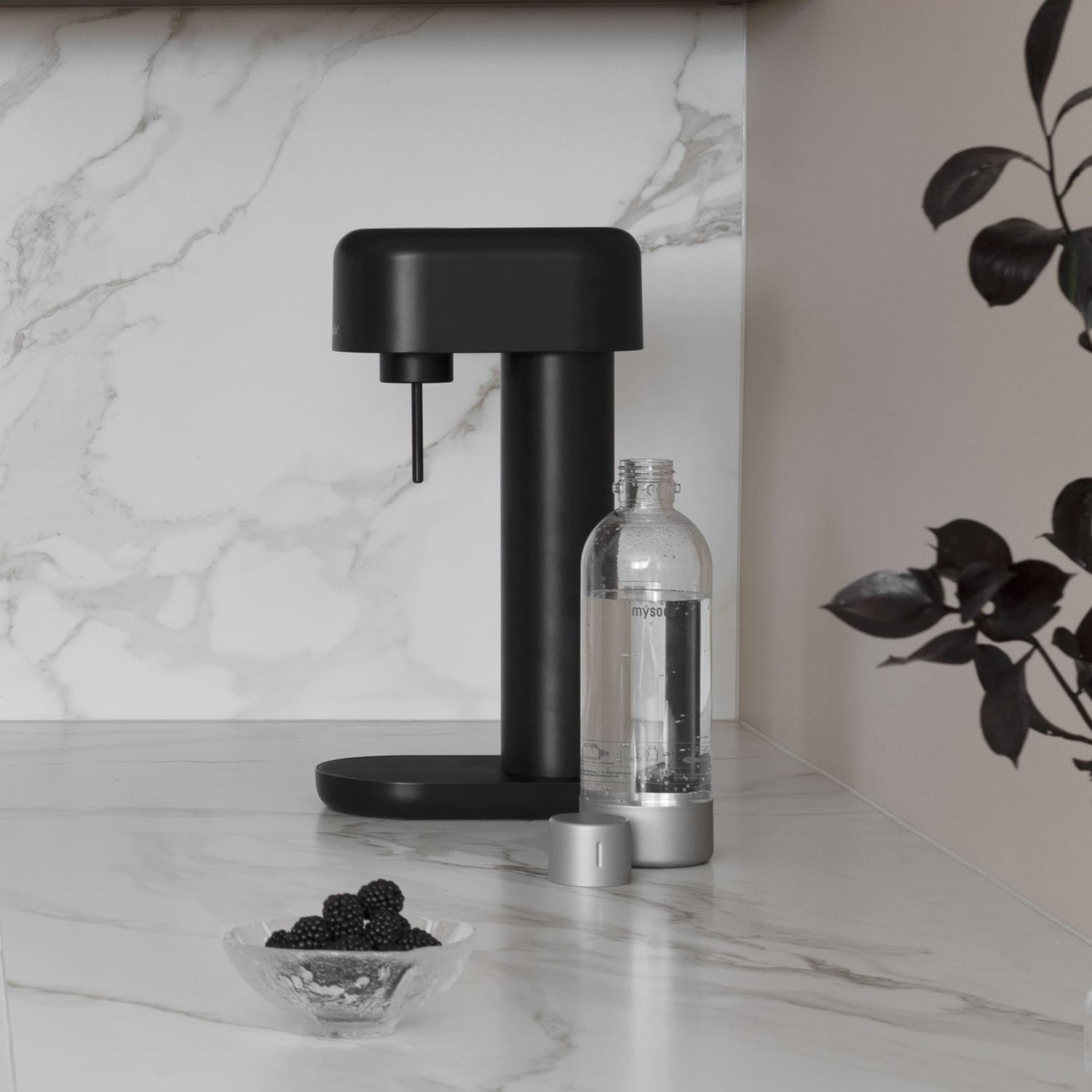 An all black Ruby 2 sparkling water maker with silver premium bottle on a hite marble kitchen counter