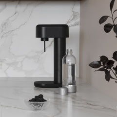An all black Ruby 2 sparkling water maker with silver premium bottle on a hite marble kitchen counter
