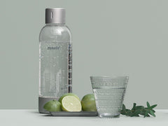 A silver premium bottle, fruit and a glass of water in front of pigeon background#väri_silver